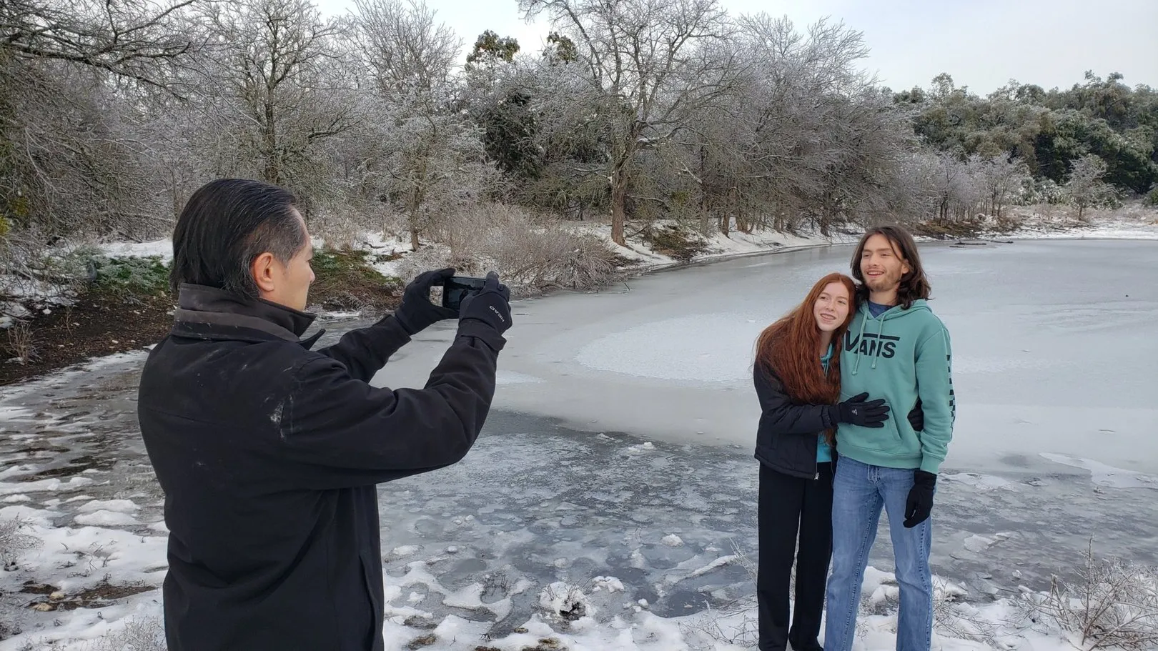 A neighbor photographing the frozen pond while two others stand at the edge of the ice.